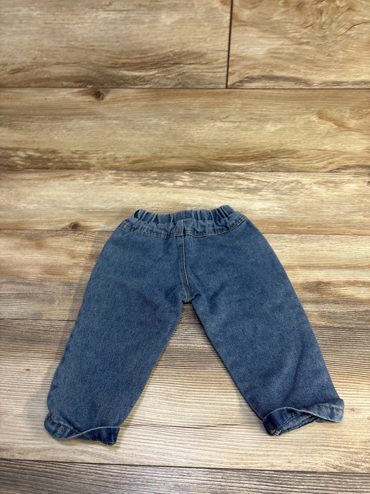 Top down view of baby blue pull on denim jeans showing elastic waistband and cuffed ankles on wood floor background