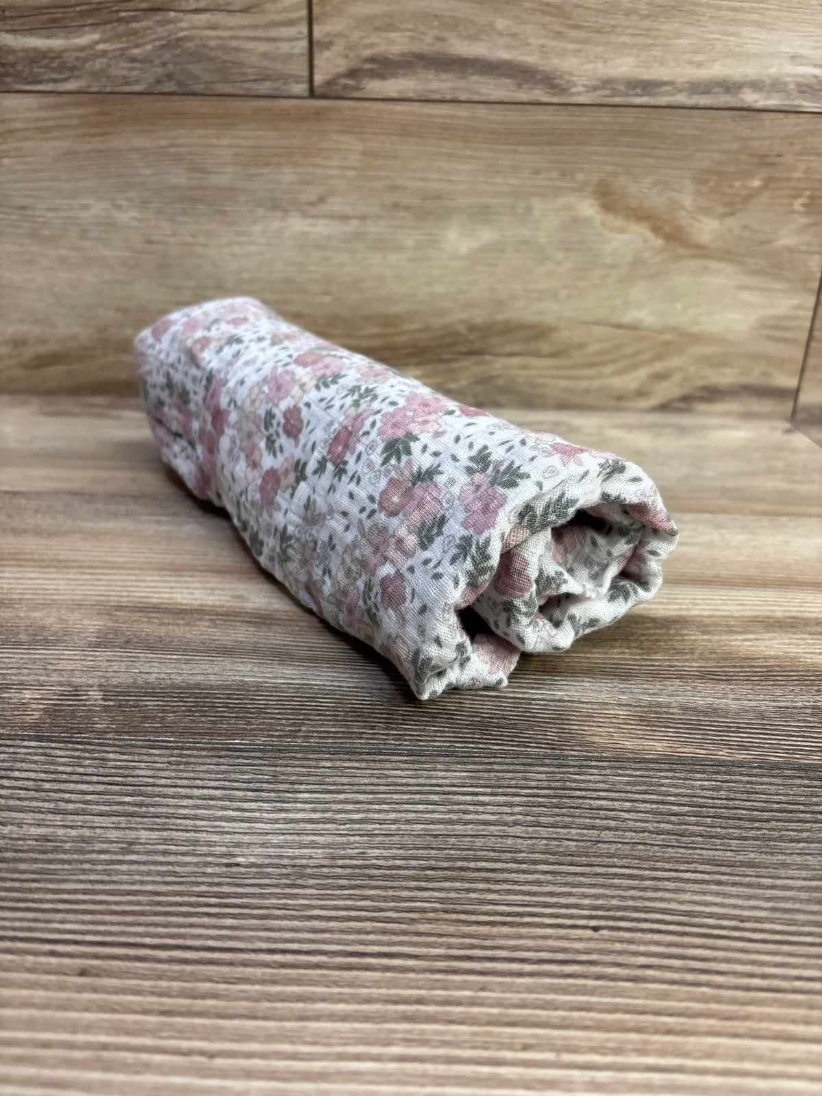 Rolled view of Modern Baby Floral Muslin Swaddle Blanket White showcasing pink floral pattern on white muslin with wood background