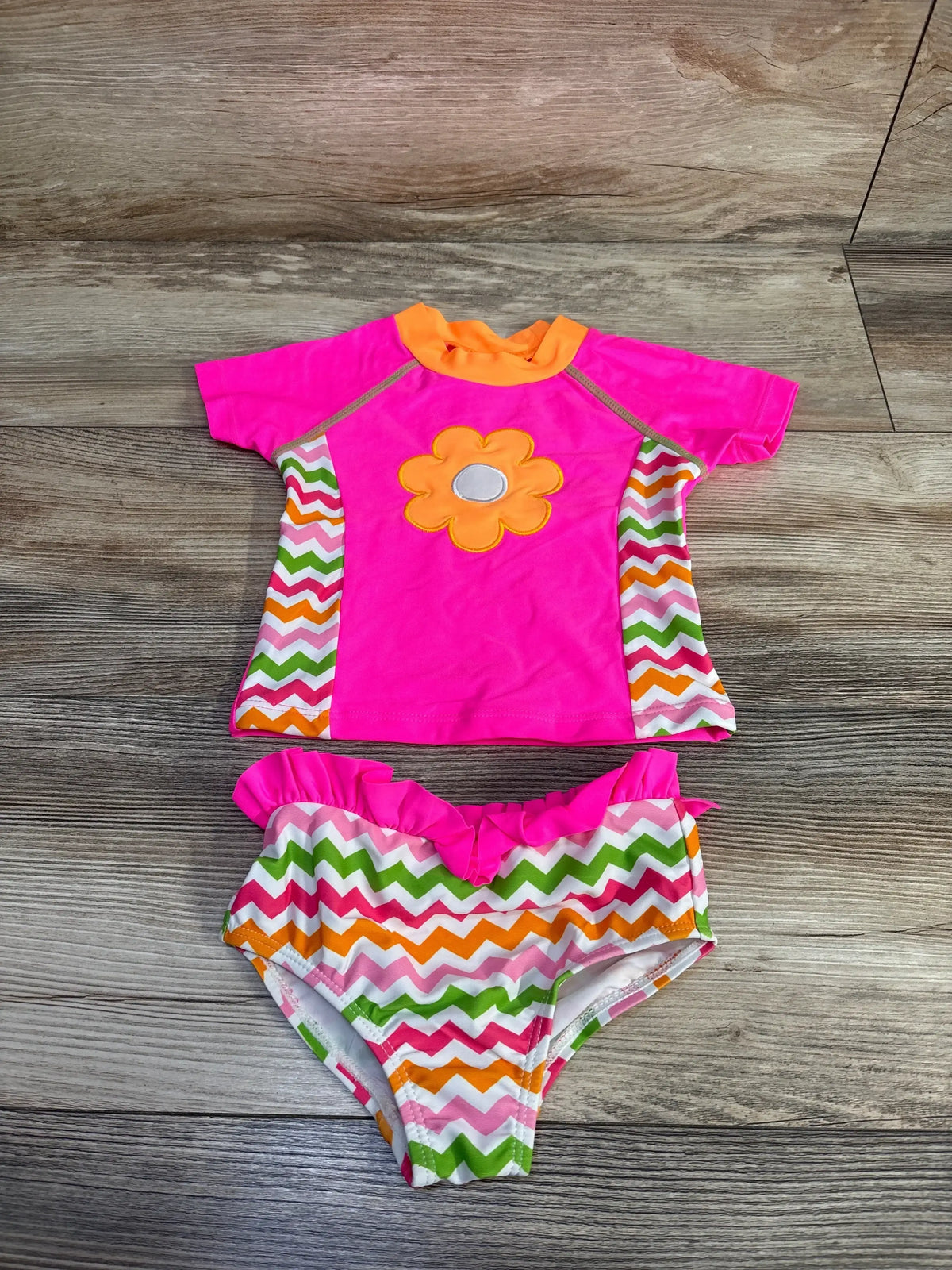 Flat lay of girls 2T pink rashguard and bikini bottoms; rashguard with orange flower and chevron sides on wood