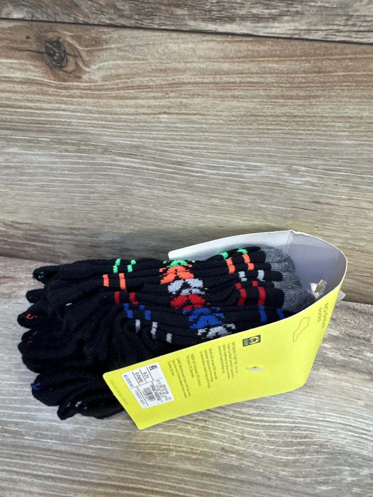 Side view of All in Motion six-pack black no-show toddler socks with multicolor stripes and yellow retail label on wood background