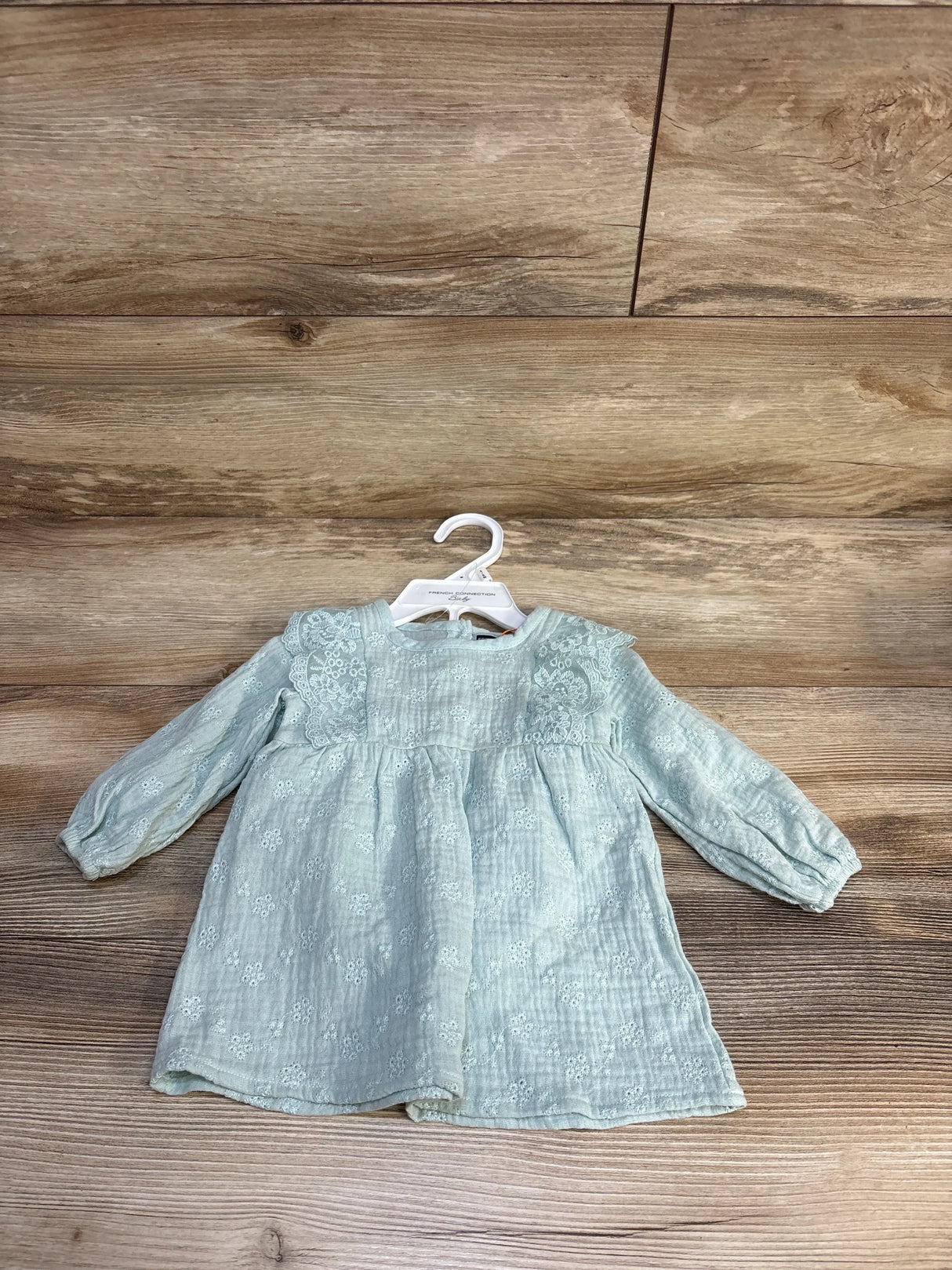 Light green long sleeve baby dress with lace detail on wooden background