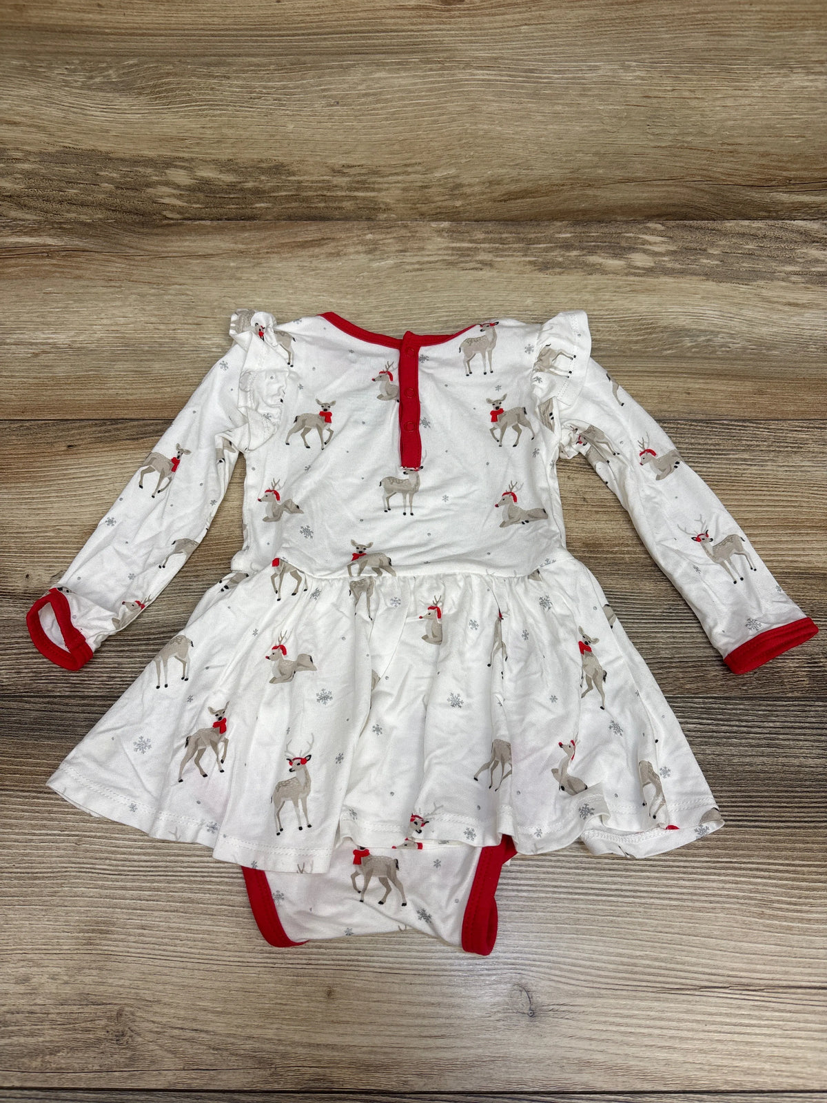 Flat lay of Kyte Baby Bamboo Cloud Deer Twirl Bodysuit Dress showcasing white reindeer print, red trim, and long sleeves on a wood surface