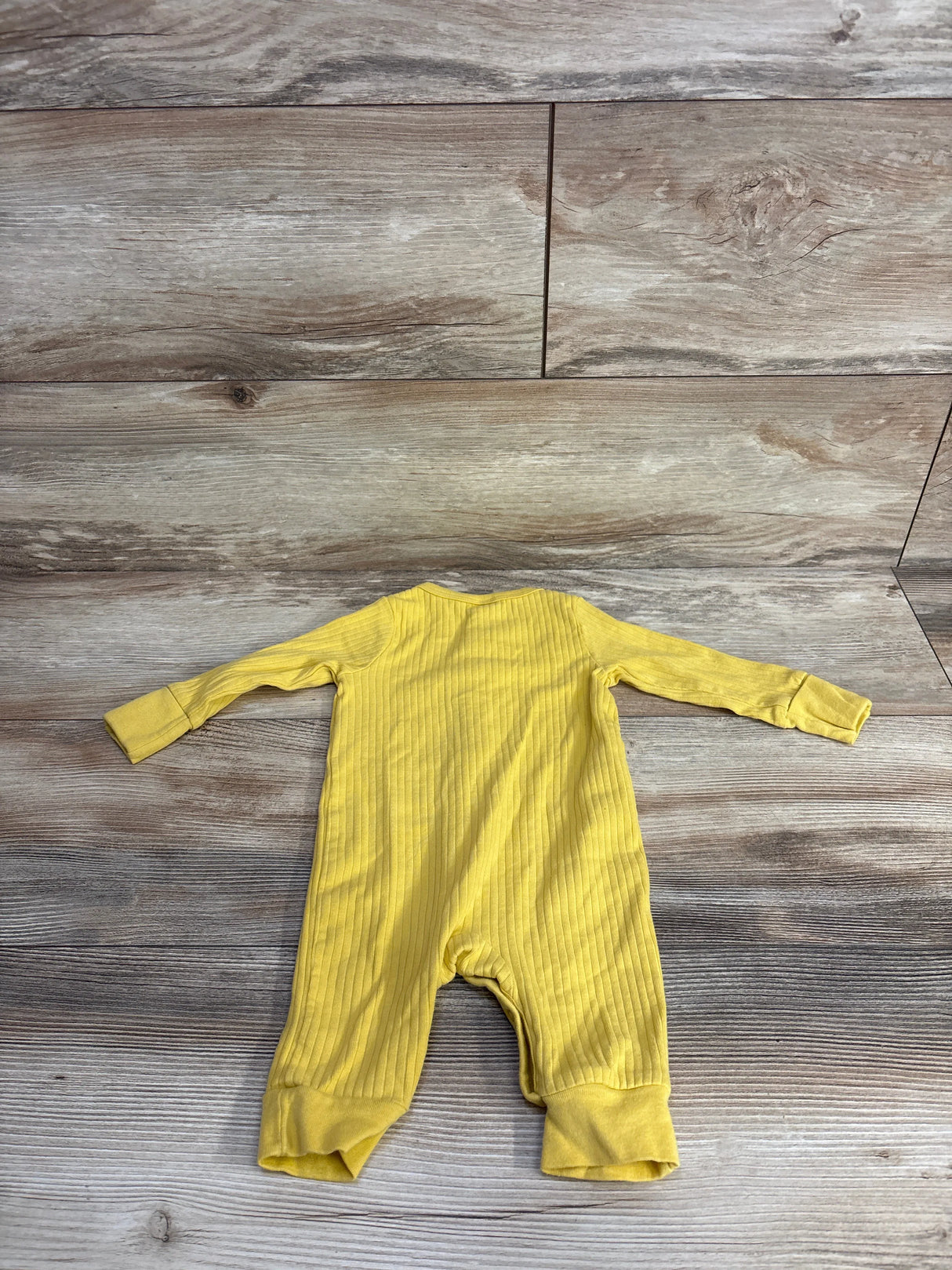 Yellow ribbed baby romper laid flat on wood floor background