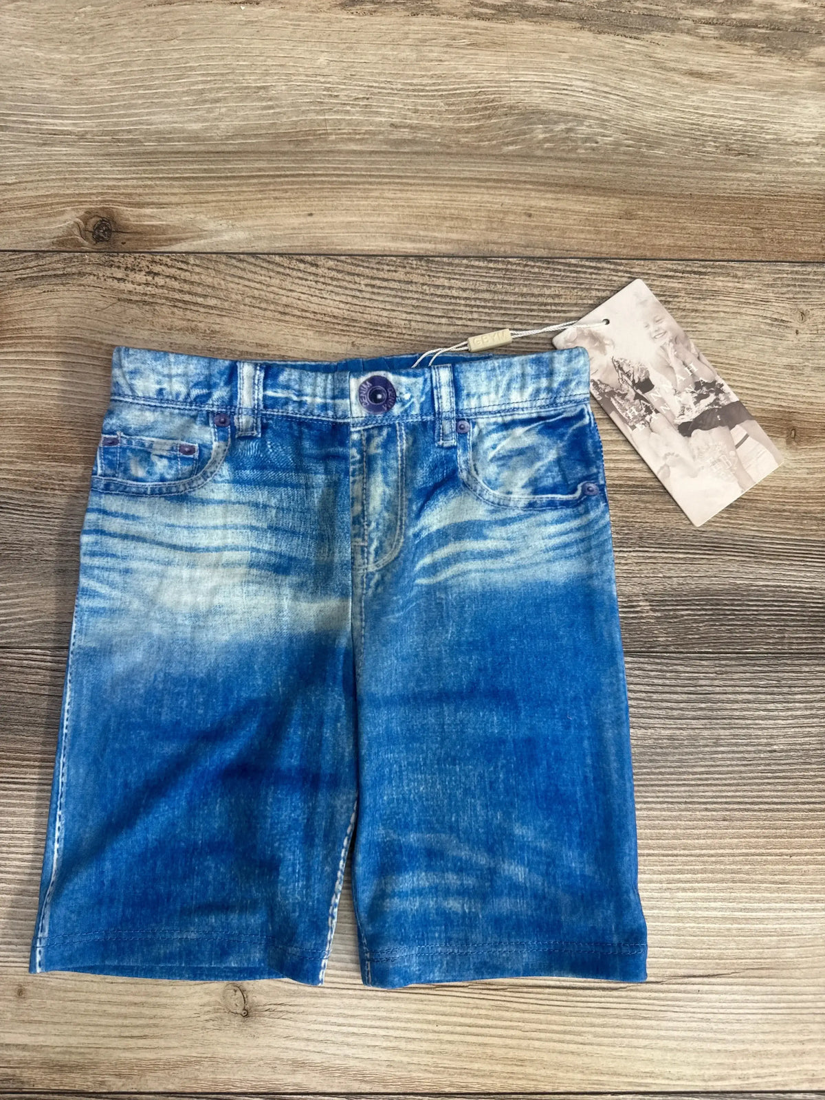 Flat lay of NEW Hanna Banana faux jean shorts in light blue denim wash with hangtag attached on wood plank floor