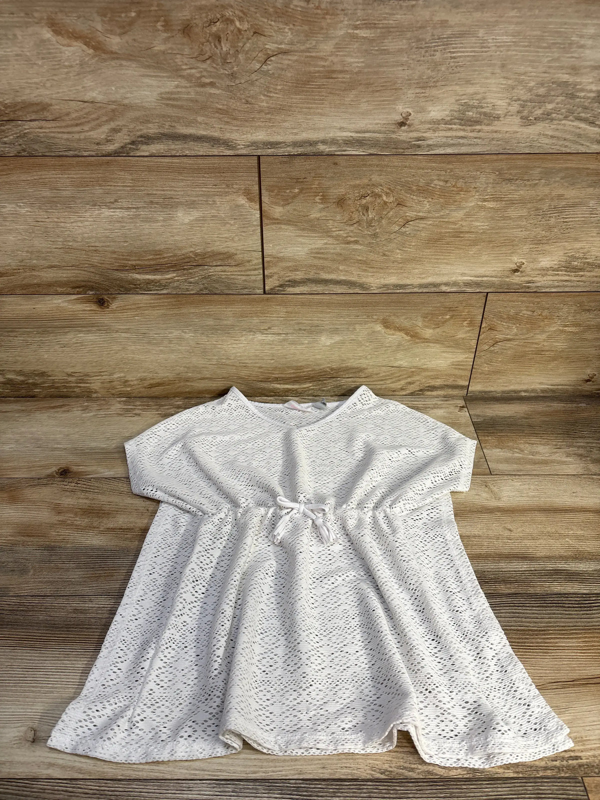 Top-down view of Children’s Place white short sleeve lace swim cover-up showcasing shirred waist and tie on wood flooring