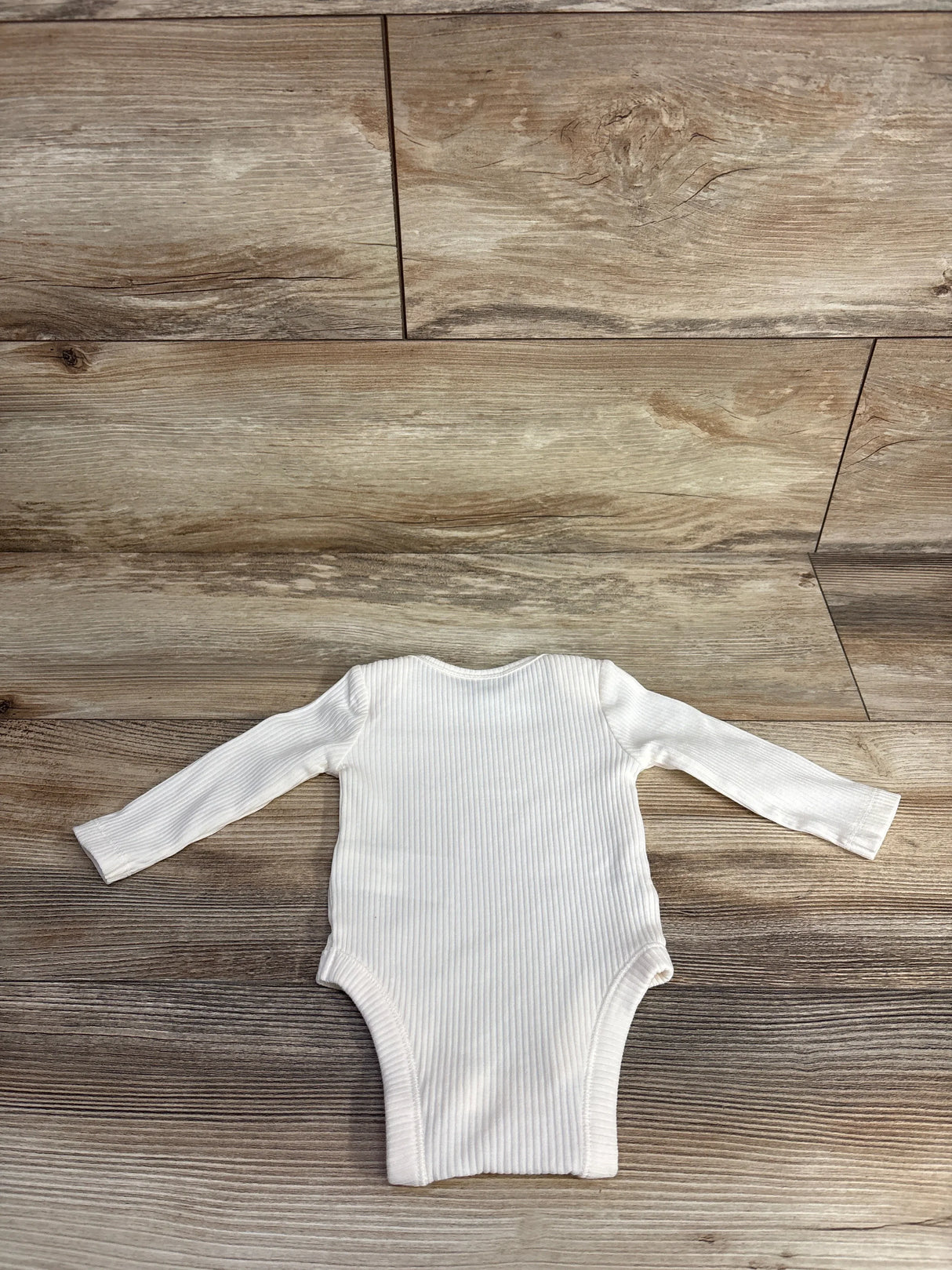 White ribbed long sleeve baby bodysuit laid flat on wood floor