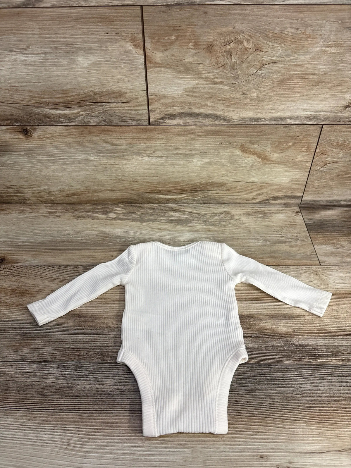 White ribbed long sleeve baby bodysuit laid flat on wood floor