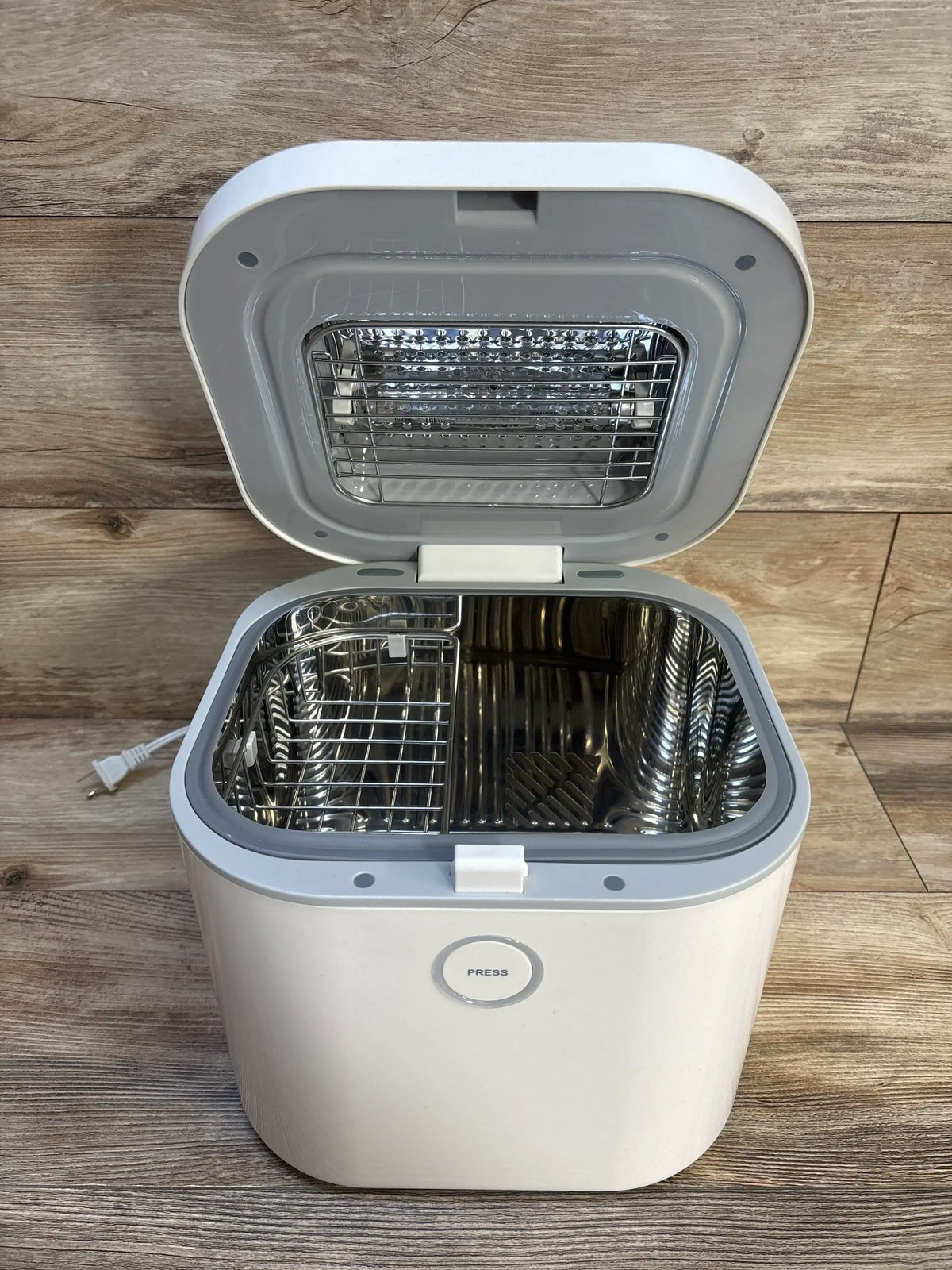 White electric sterilizer for baby bottles with open lid and metal basket on wood floor