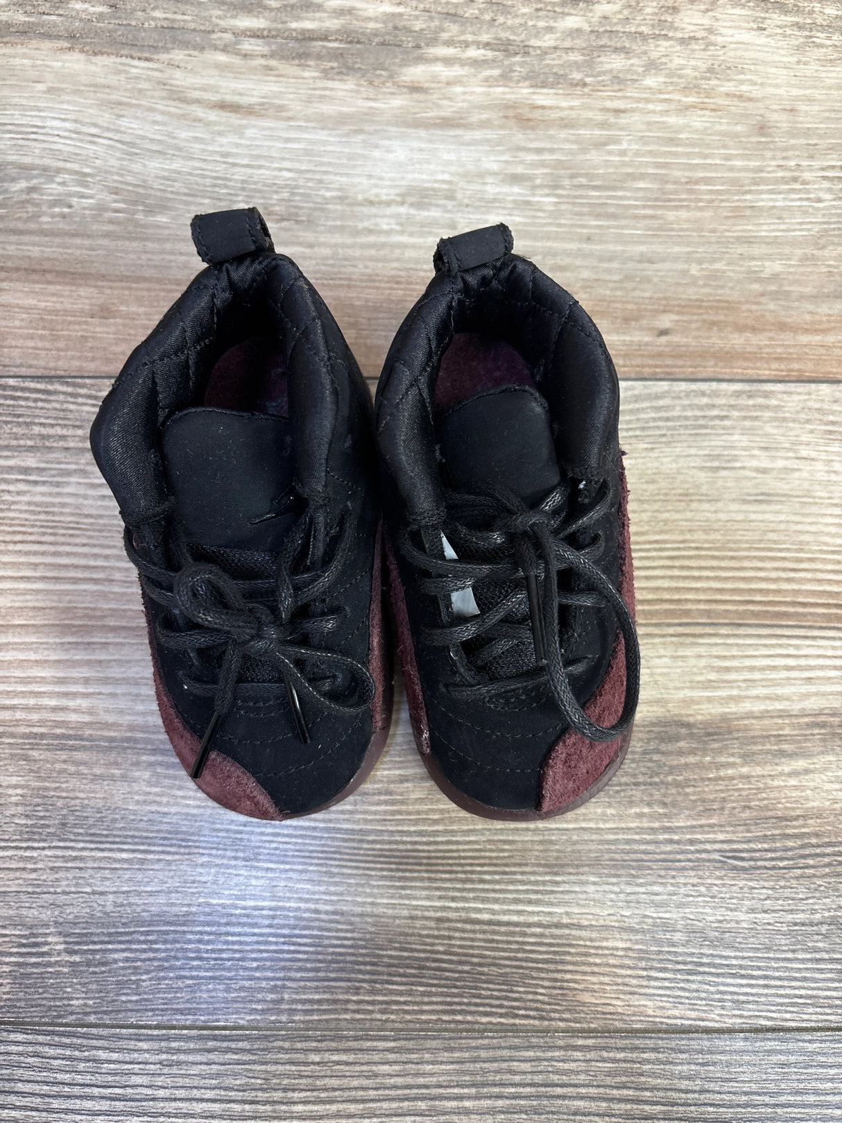 Black and maroon baby sneakers with laces on wood background