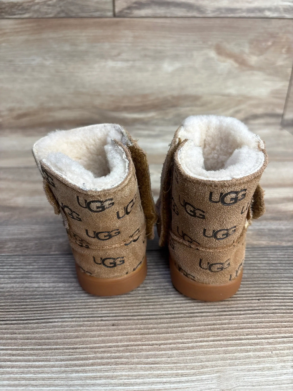 Pair of toddler UGG boots in chestnut suede with branded logo and shearling lining on wooden floor