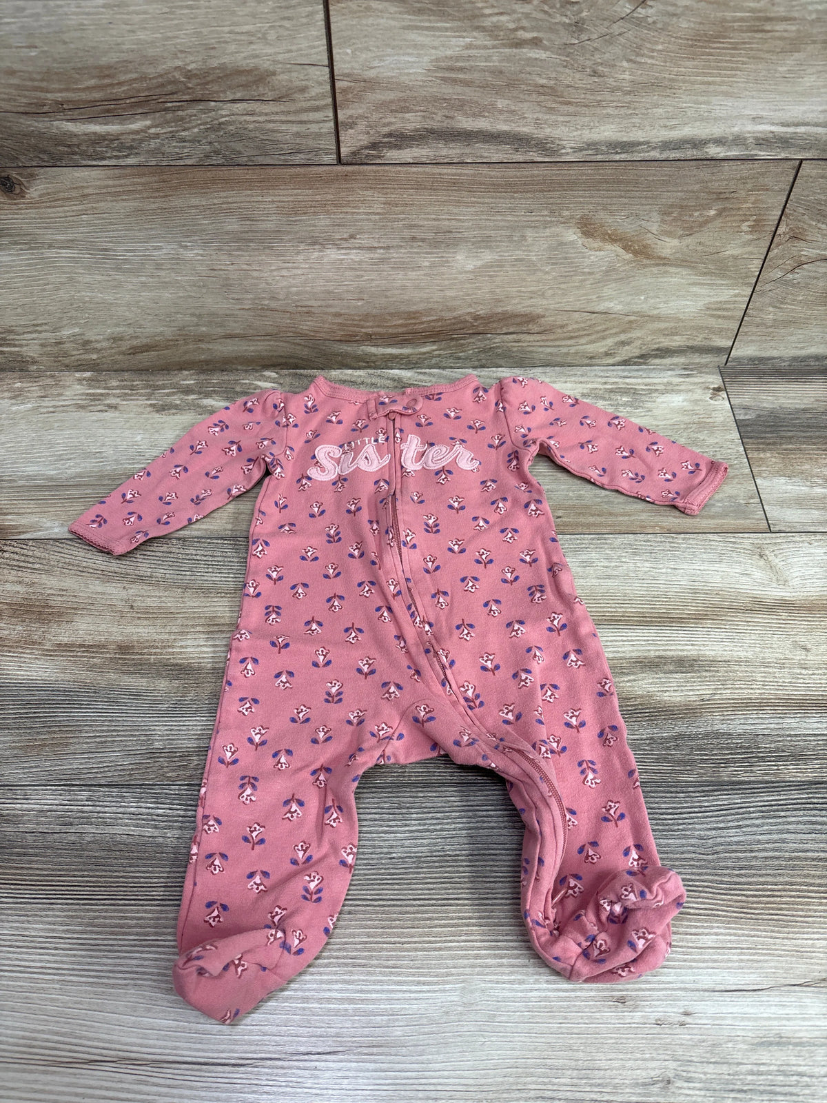 Pink floral baby sleeper with 'Sister' text on the chest, laid flat on a wooden background.