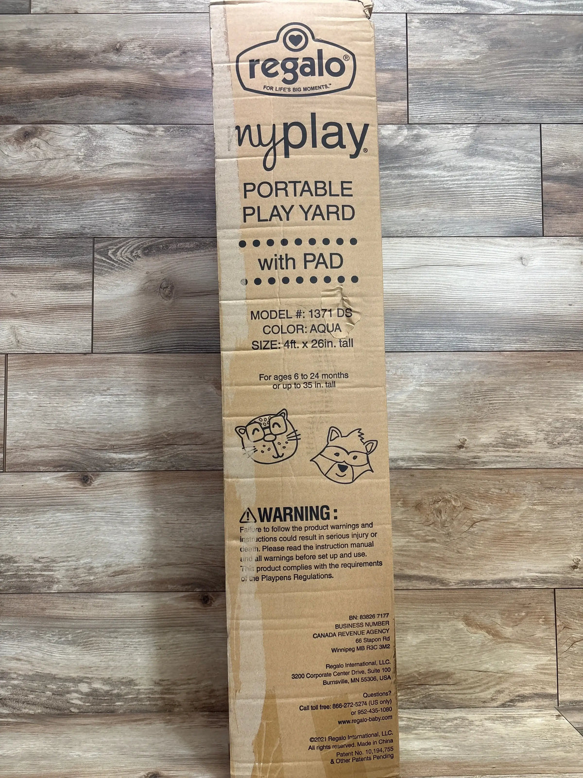 Front of Regalo MyPlay play yard box showing Portable Play Yard with Pad headline, model 1371 DS, aqua, 4ft x 26in, on wood floor