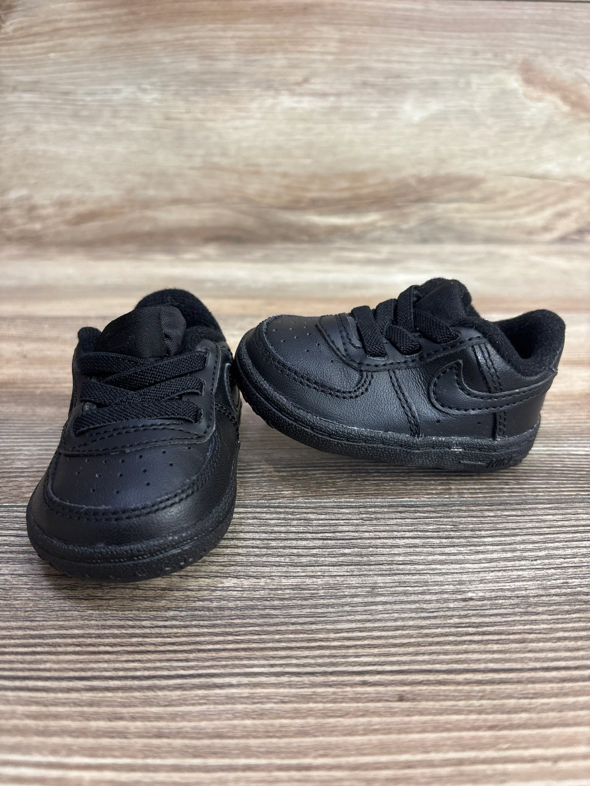 Pair of black toddler Nike sneakers with laces on wooden surface, children's resale shoes