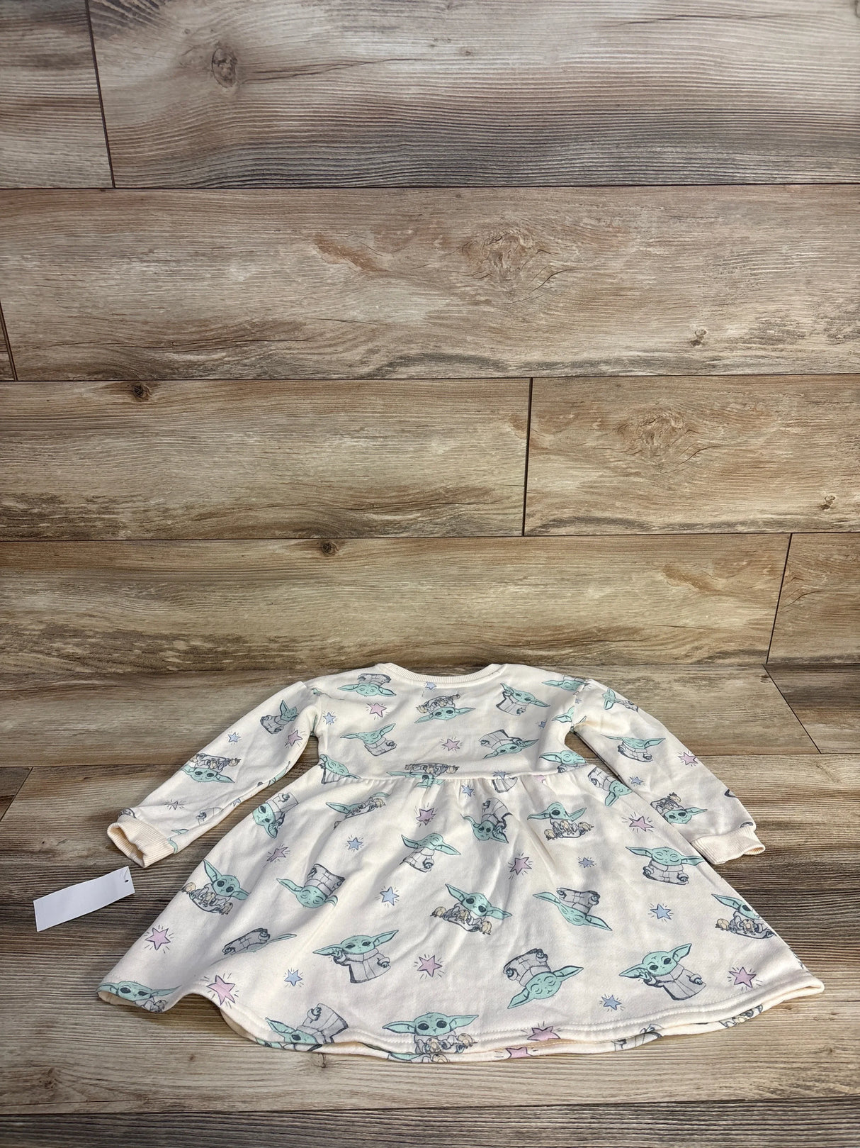 Front view of NEW Star Wars sweater dress in cream showcasing Baby Yoda print and long sleeves with hangtag on wood plank floor