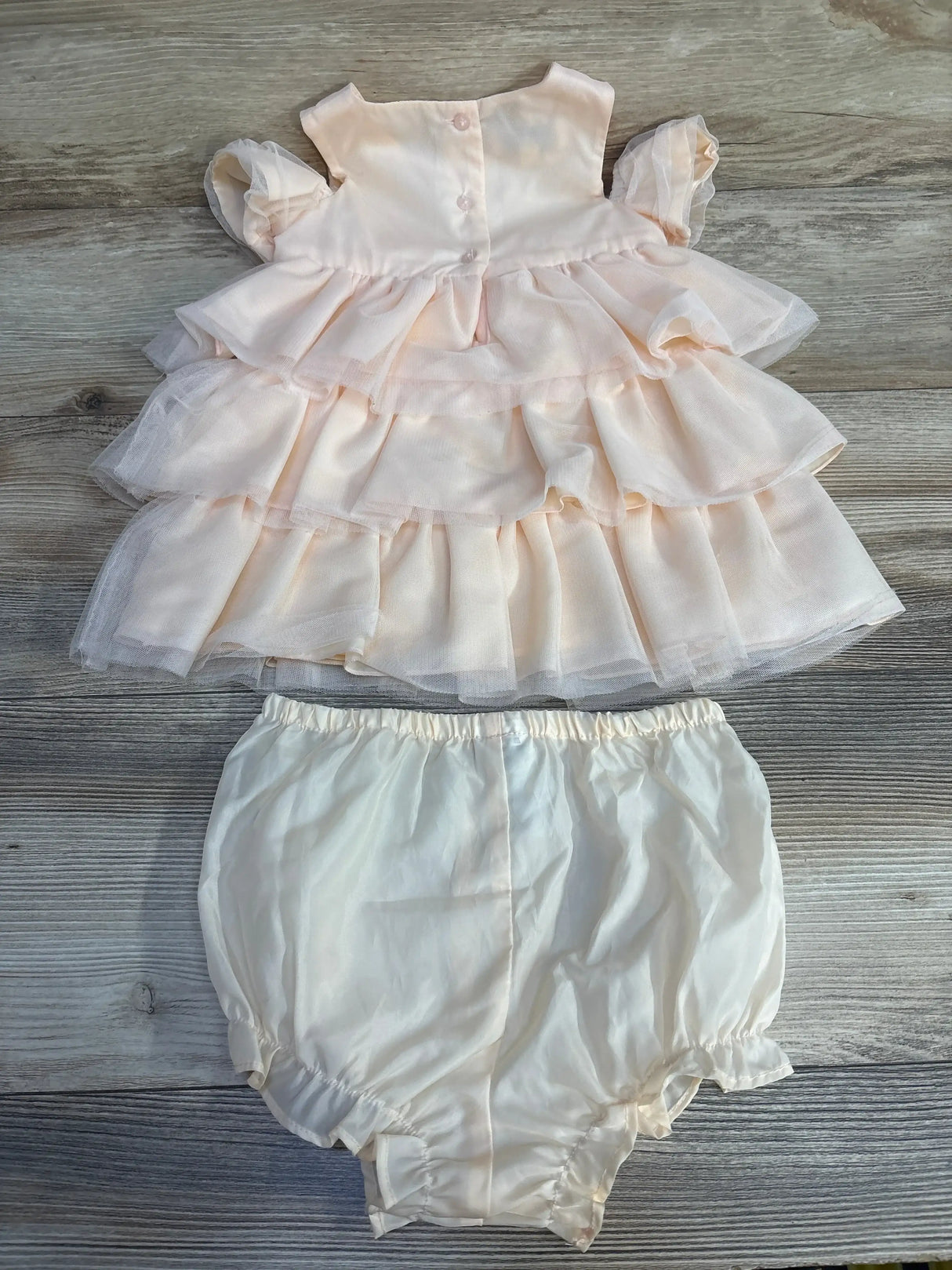 Flat lay of peach tiered baby dress with matching bloomers, 18mo, showing ruffled tiers and button-back on wood