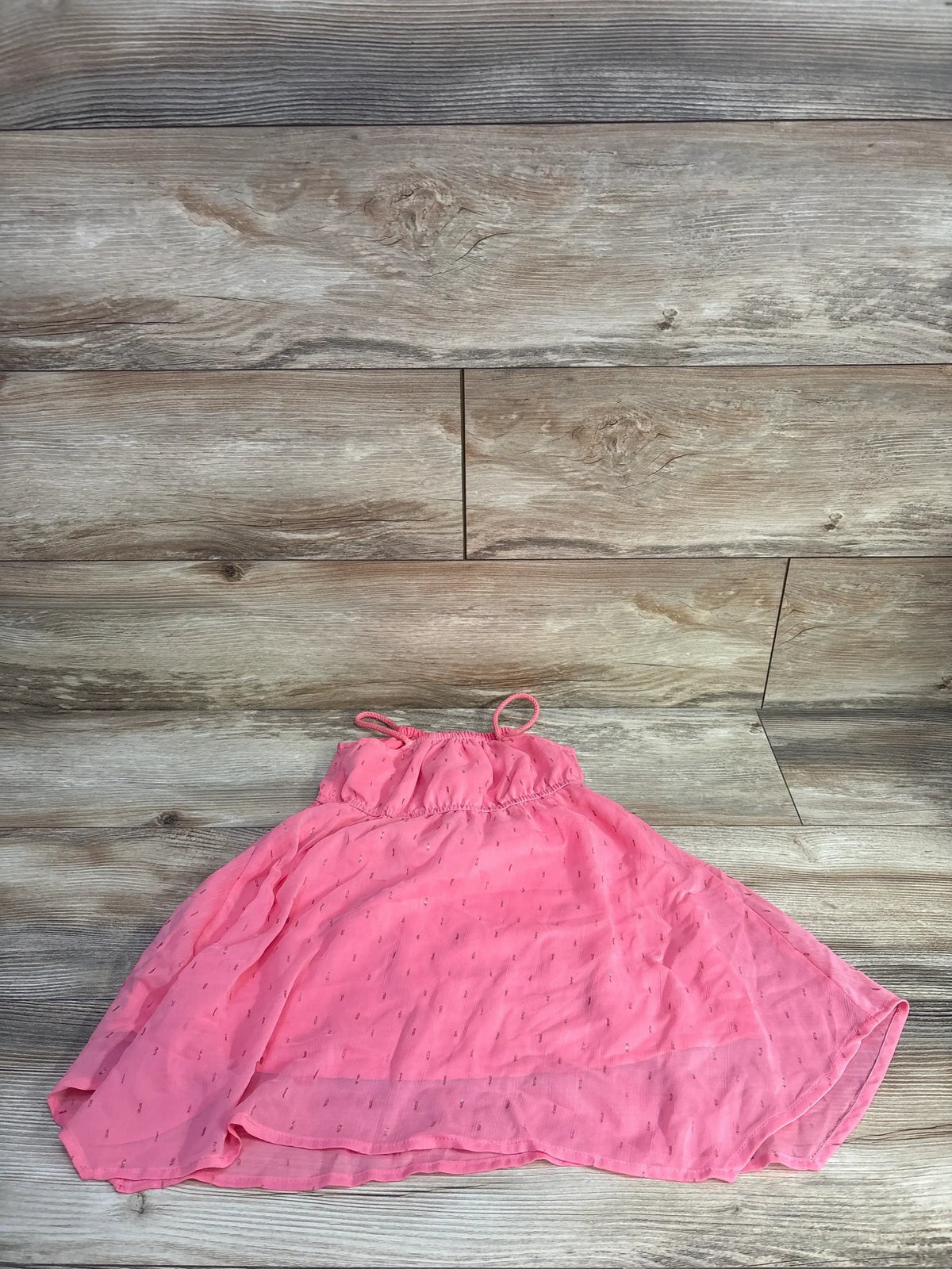 Flat lay of H&M asymmetric pink chiffon dress (2T) showing uneven hem, gathered bodice and thin straps on wood background