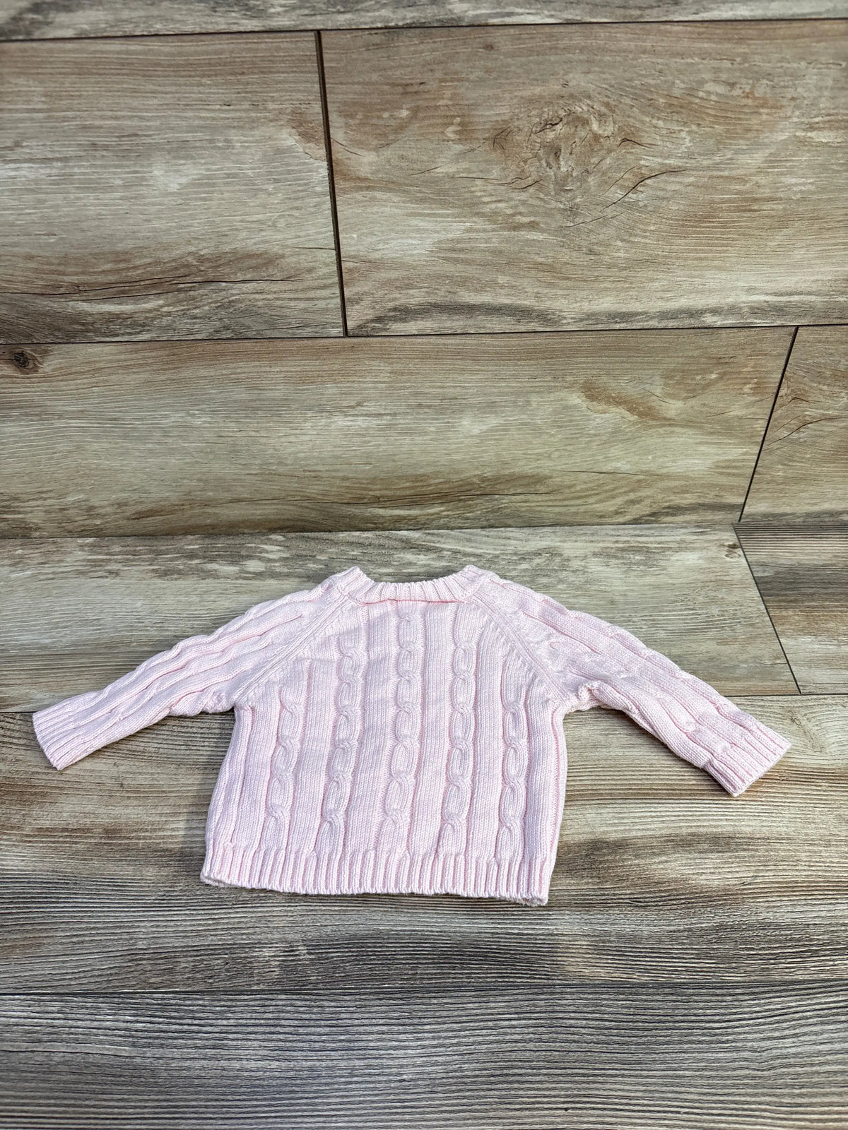 Elegant pink cable knit baby cardigan for 0-6 months on a rustic wood background
