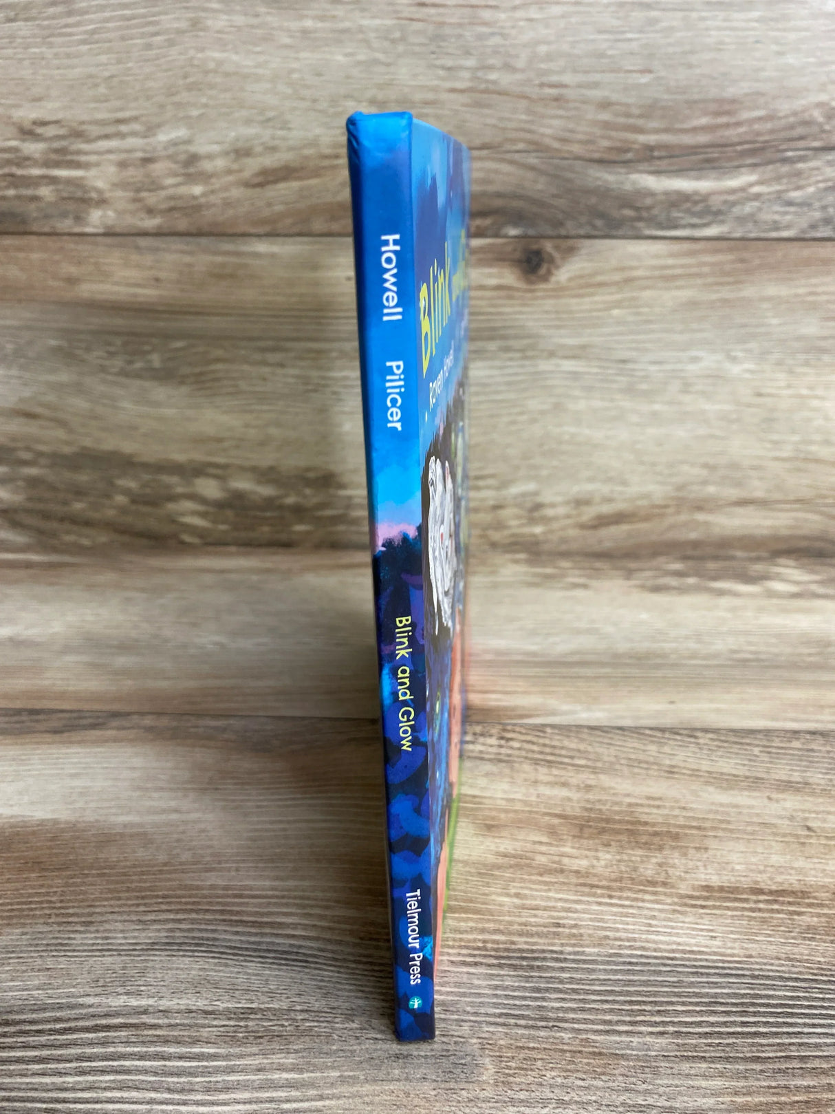 Children's book spine titled 'Blink and Glow' by Howell and Pilcer on wood background