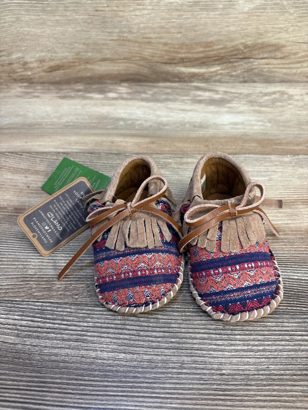 Patterned baby moccasins with fringe and laces on wooden background, baby shoes resale