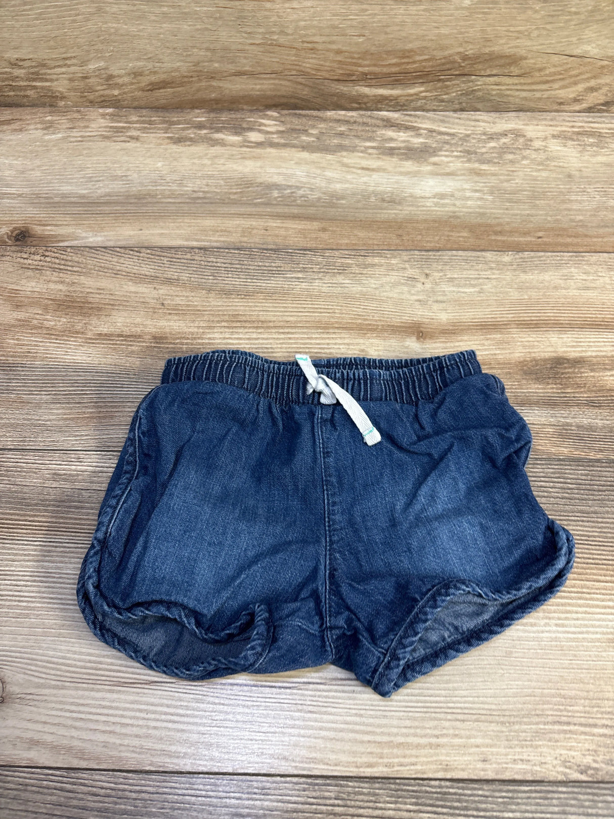 Flat lay of Cat and Jack chambray toddler shorts showing elastic waistband, white drawstring and rolled hems on wood, size 3T