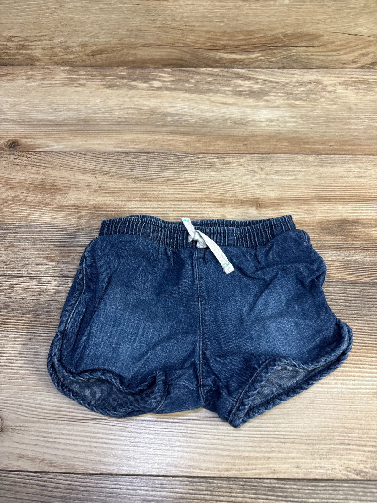 Flat lay of Cat and Jack chambray toddler shorts showing elastic waistband, white drawstring and rolled hems on wood, size 3T