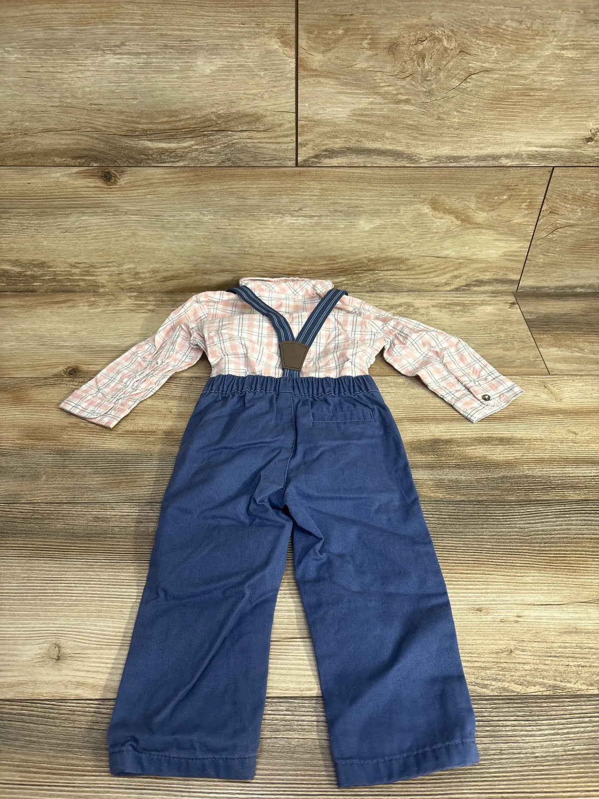 Plaid long-sleeve shirt with blue suspender pants for kids on wood background