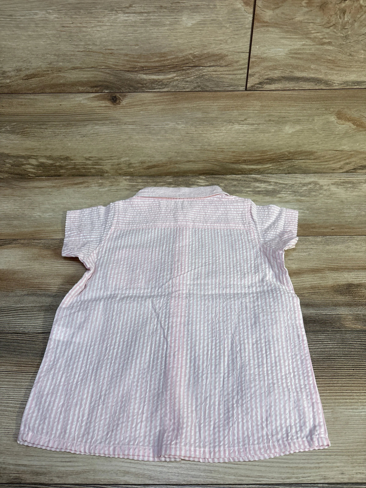 Back view of Monica + Andy pink striped seersucker button-up shirt in size 5T laid flat on a wood surface