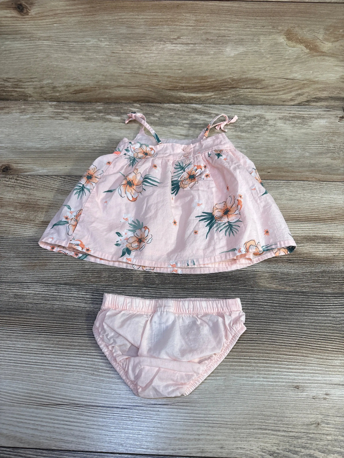 Top-down view of Oshkosh two-piece tank top and bloomers set showcasing its pink floral print on a wood surface
