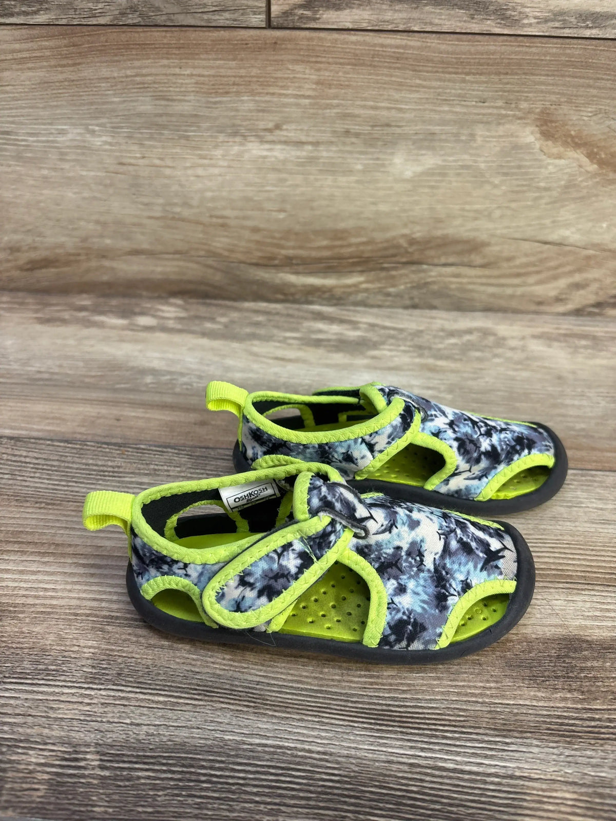 Front view of OshKosh aquatic water shoes, size 7C, in grey and green with hook and loop closure on a wood floor