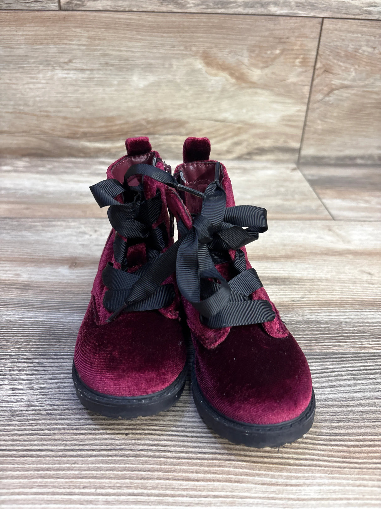 Front view of Cat and Jack burgundy velvet toddler ankle boots showcasing black ribbon laces with wood plank background