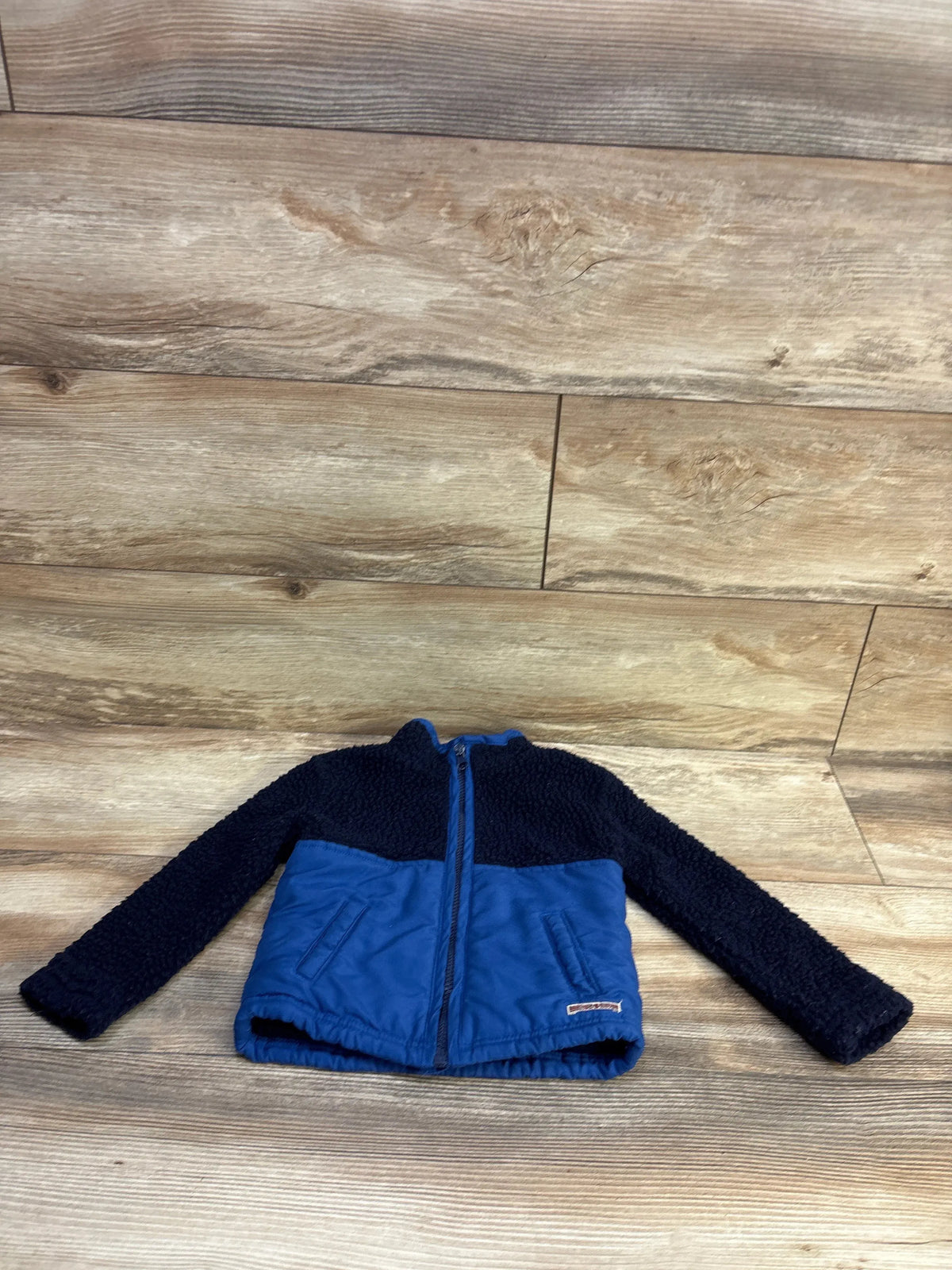 Front flat lay of Hudson Sherpa jacket showing navy sherpa top, blue lower body, full zip and side pockets on wood floor