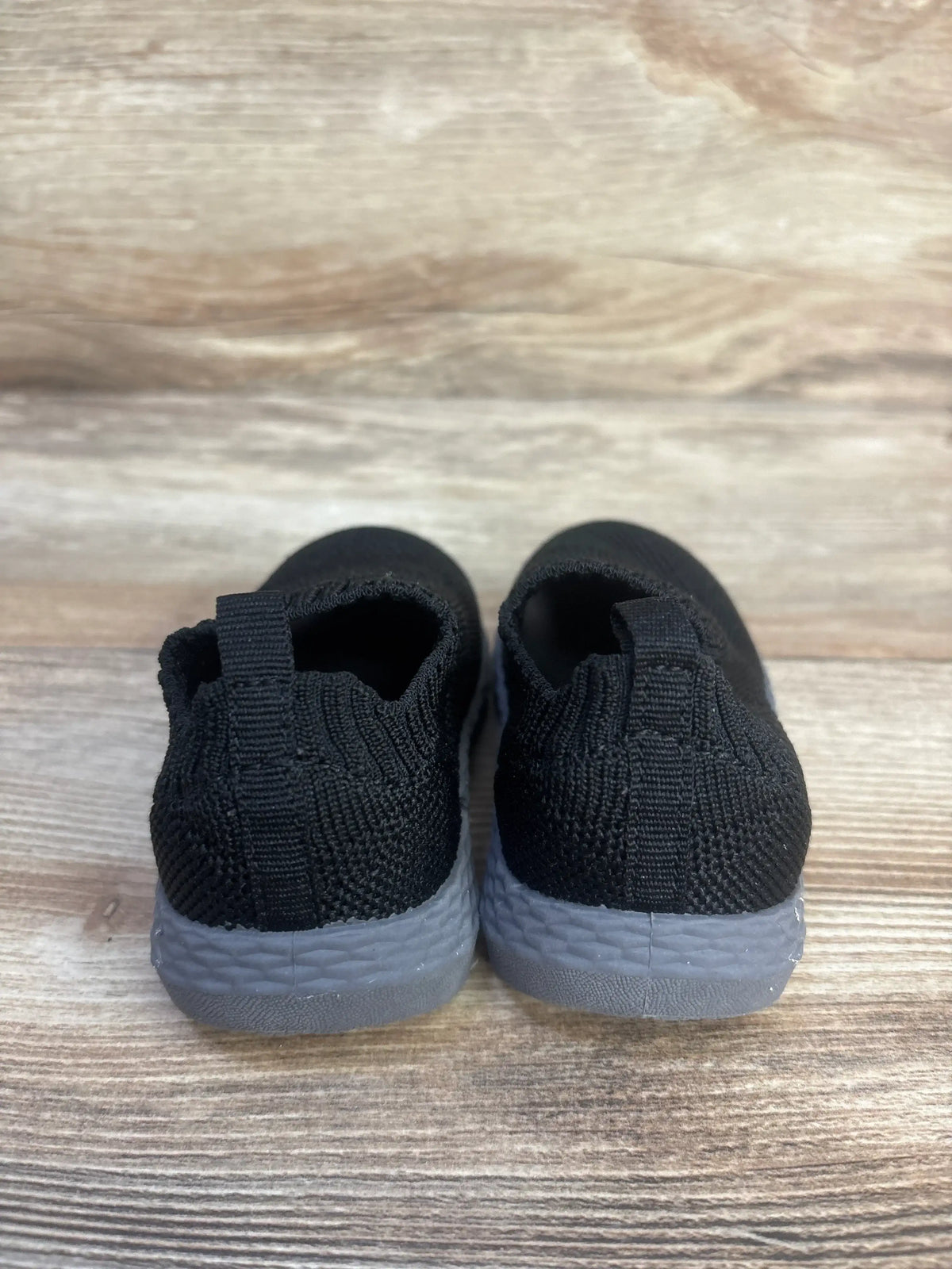 Rear view of Carter’s Taylen pull-on athletic sneakers showcasing black knit uppers and gray soles on a wood surface