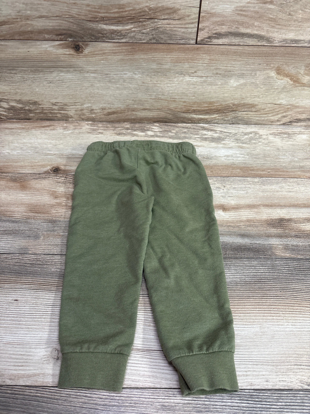 Front view of Carter’s green pull-on drawstring joggers in size 3T showcasing elastic waist and ribbed cuffs on a wood-grain background