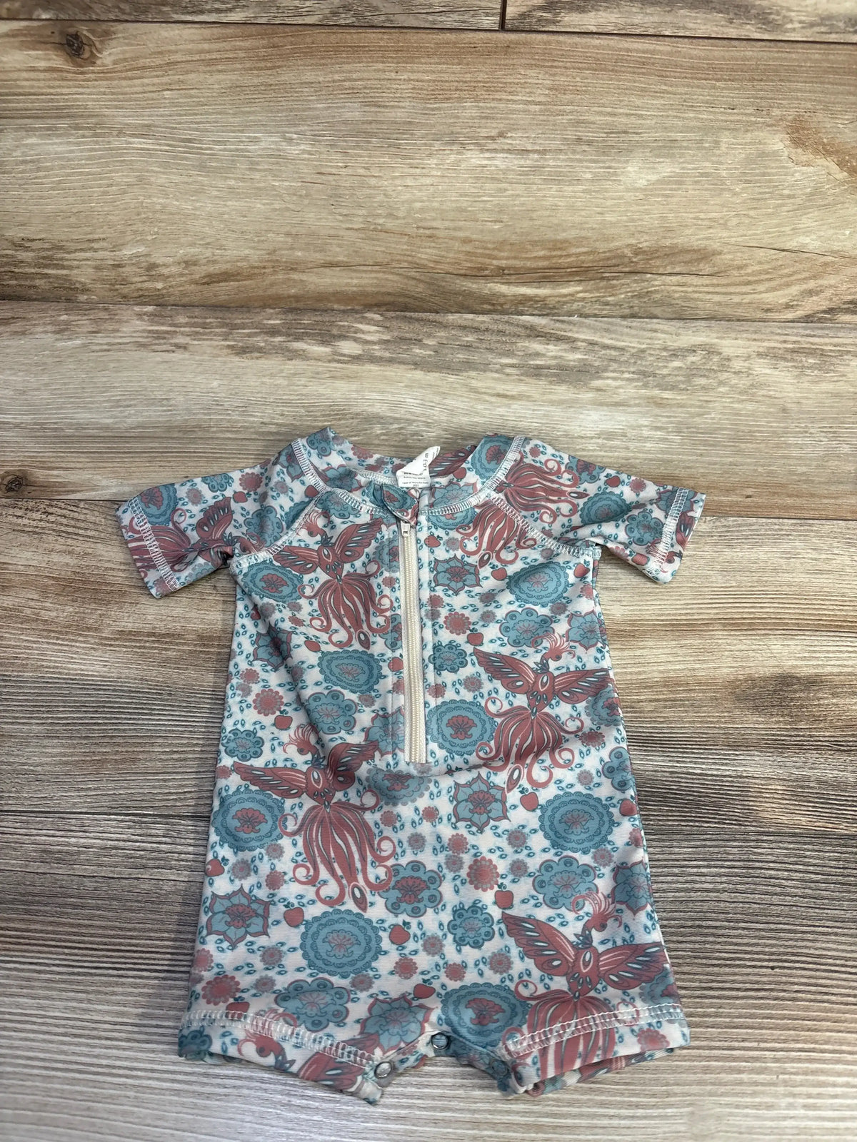 Flat lay of Kate Quinn zip-front rash guard shortie showing front zipper and octopus floral print on wood background