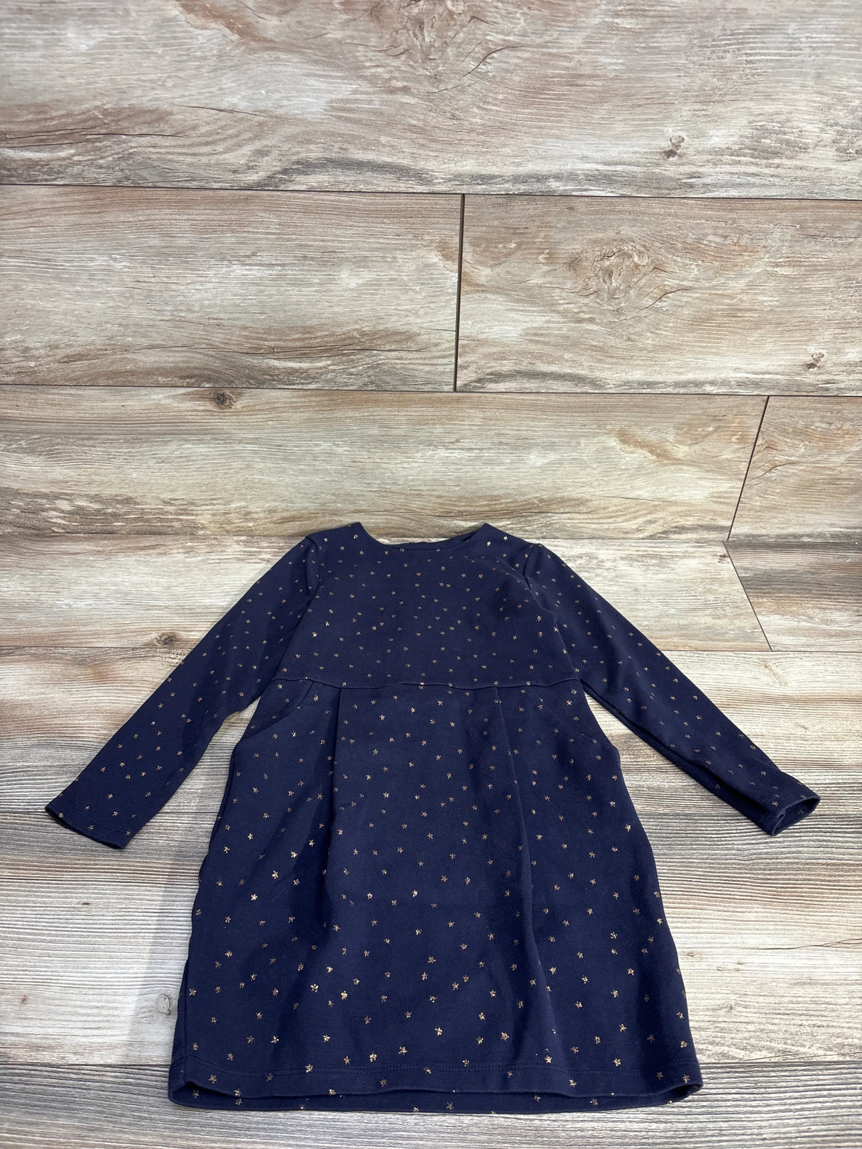 Navy blue long sleeve girls dress with gold star print, laid flat on wood background