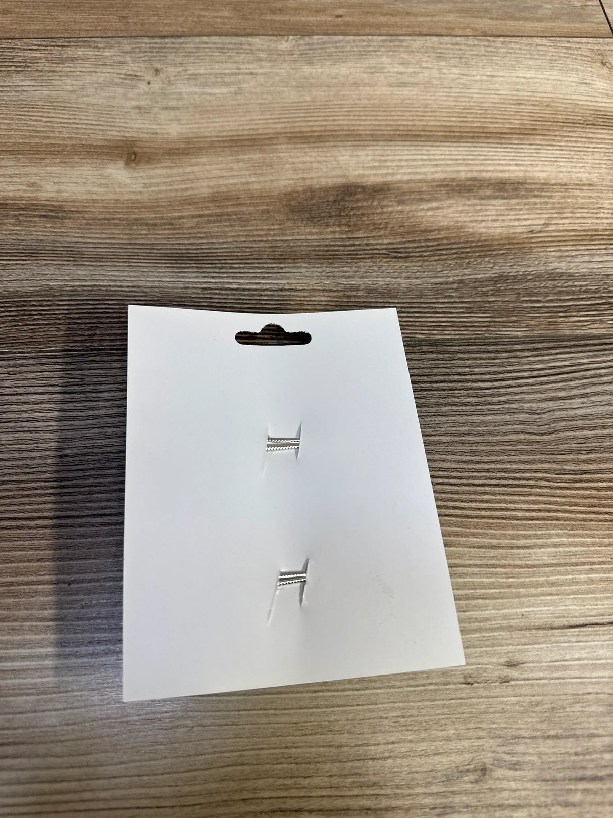 Silver kids' earrings on white card, wood floor background