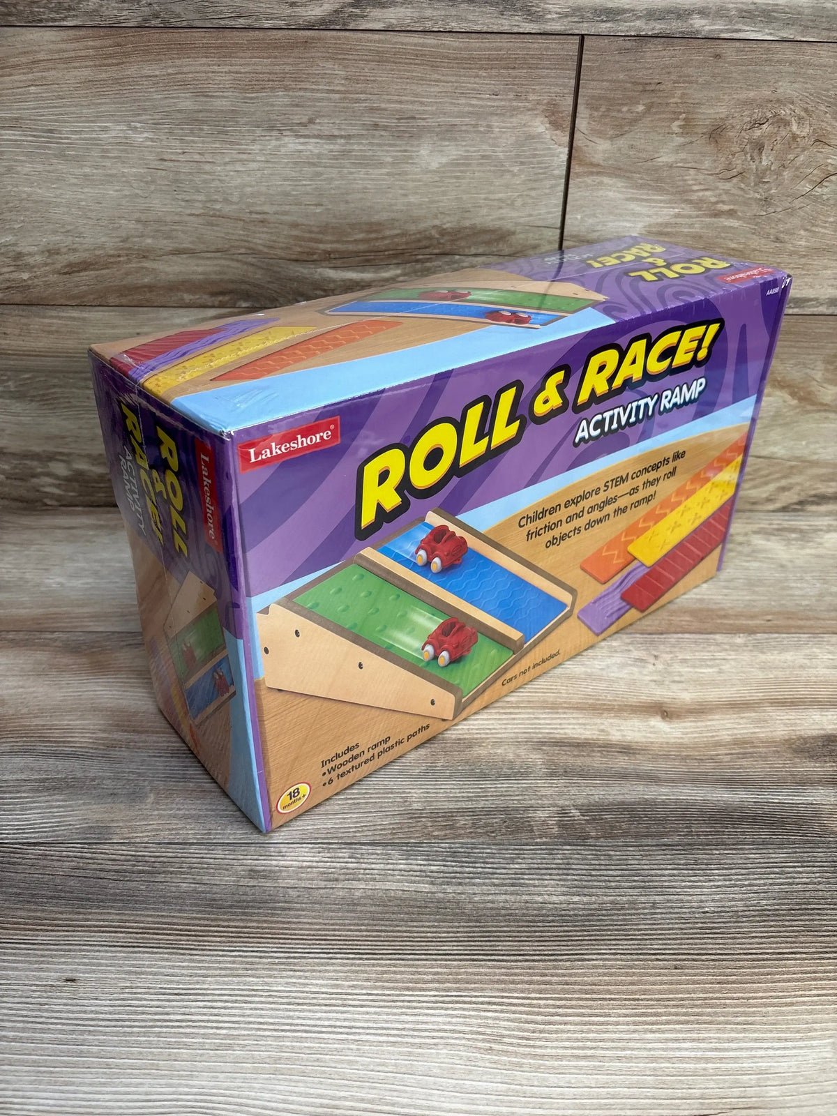 Angled view of Lakeshore Roll and Race box with large Roll and Race headline, two red toy cars and textured ramp inserts on a wood tabletop
