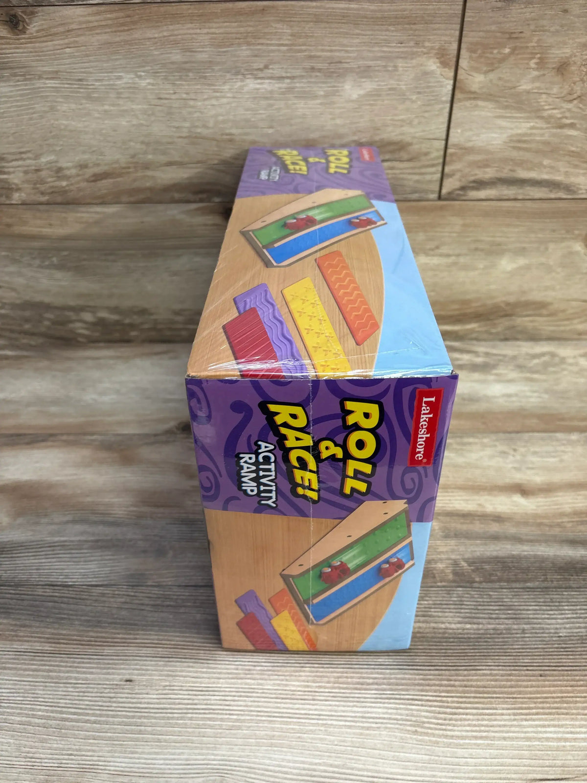 Angled front view of Lakeshore Roll and Race Activity Ramp box showing colorful packaging and textured ramp strips on wood