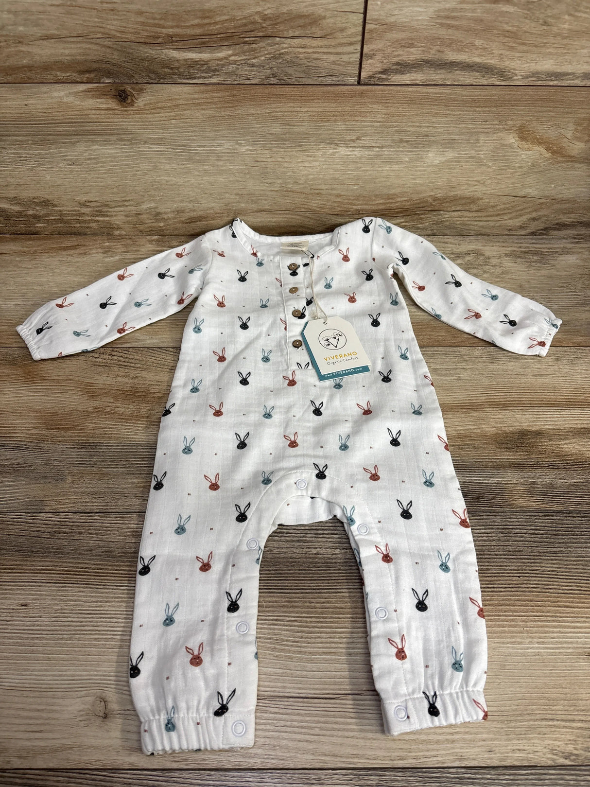 White baby romper with multicolor bunny prints, long sleeves, wooden buttons, on wood background.