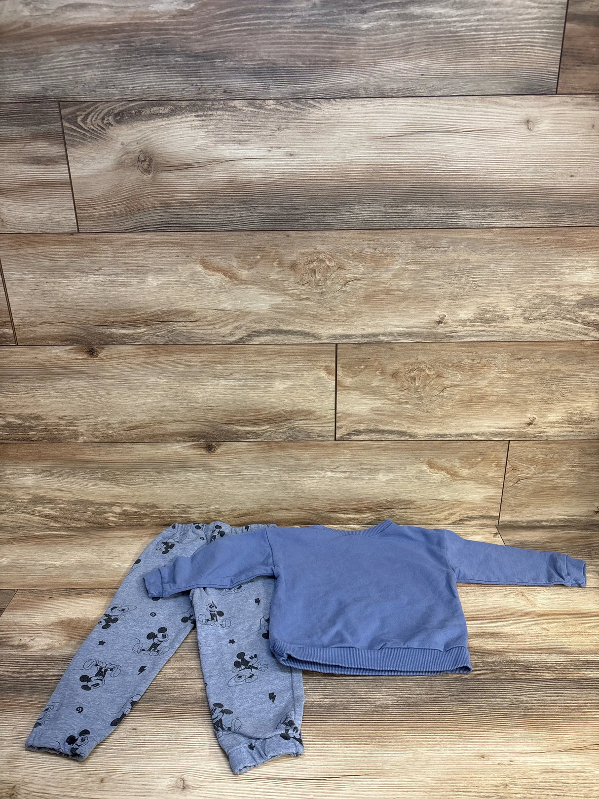Blue toddler sweatshirt and grey Mickey Mouse print pants on wood background