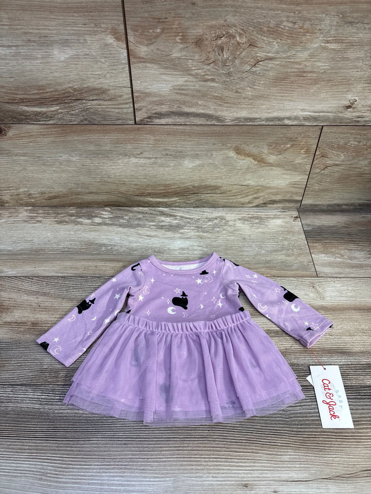 Flat lay of newborn purple Halloween tulle dress with cat and moon print and layered skirt on wood background
