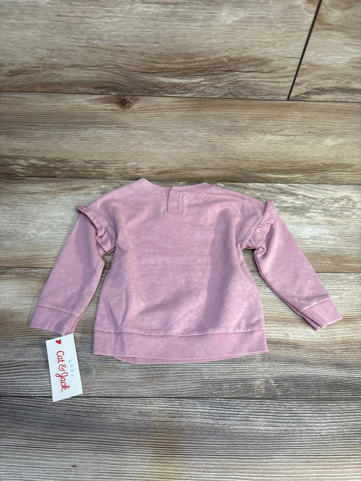 Light pink long sleeve baby sweatshirt with ruffle shoulder detail on wooden background