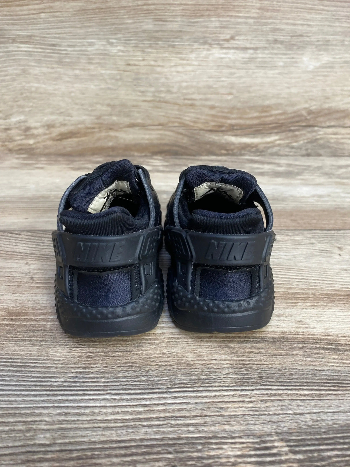 Rear view of Nike Air Huarache Run toddler sneakers showing molded heel strap with NIKE logo on wood background, size 5C