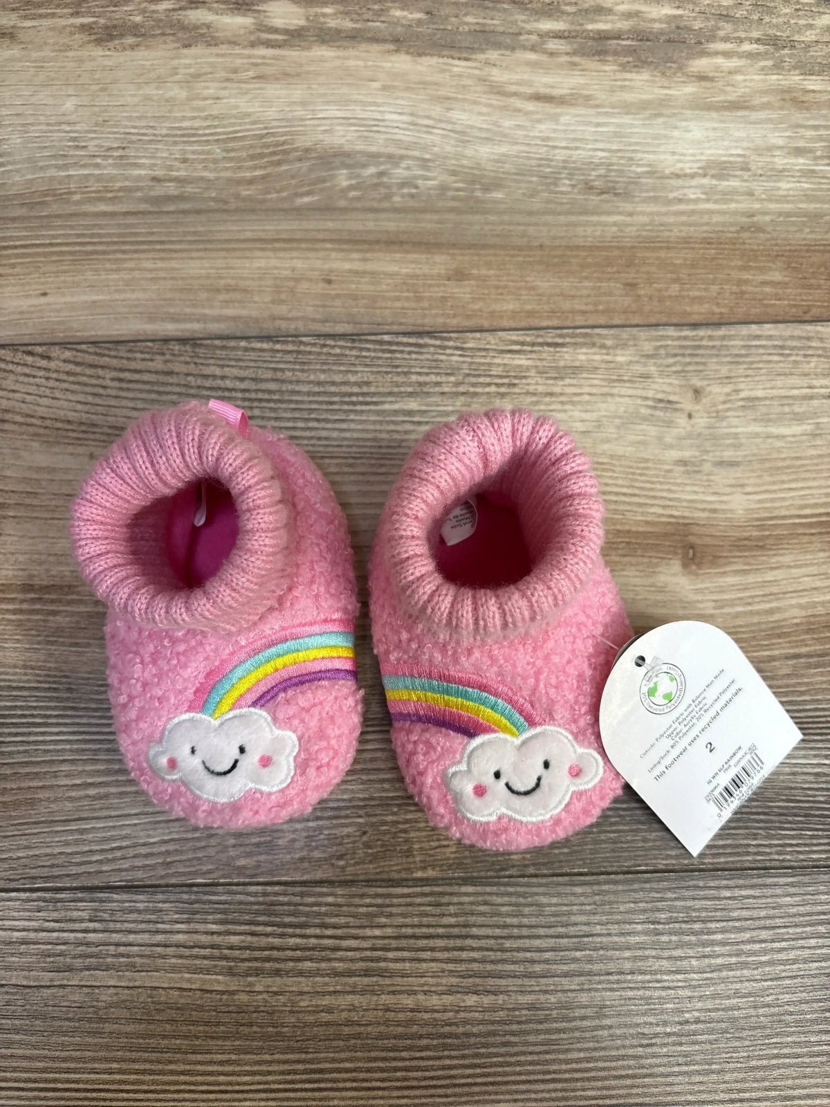 Pink baby booties with smiling cloud and rainbow patches on wood background
