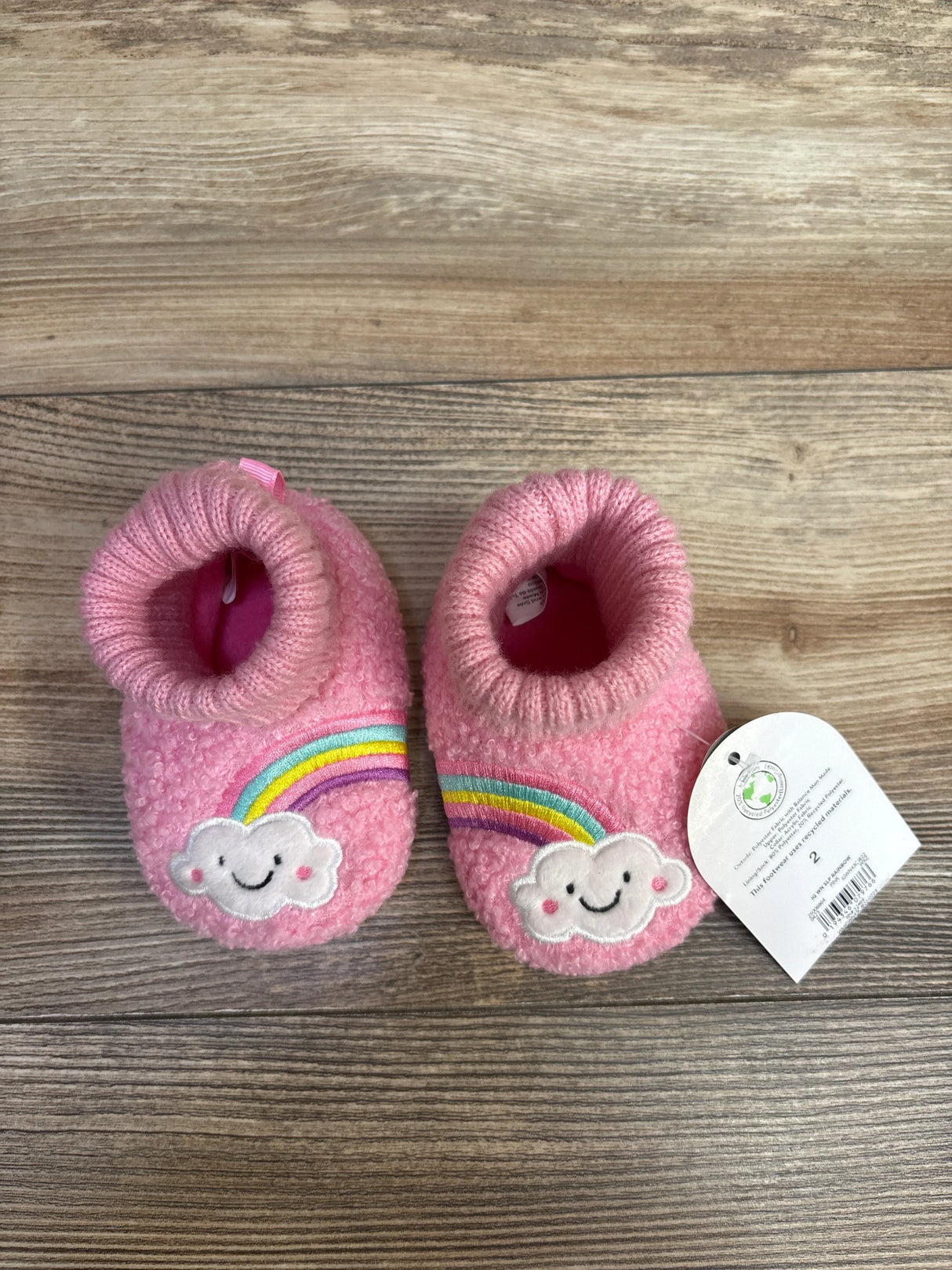 Pink baby booties with smiling cloud and rainbow patches on wood background
