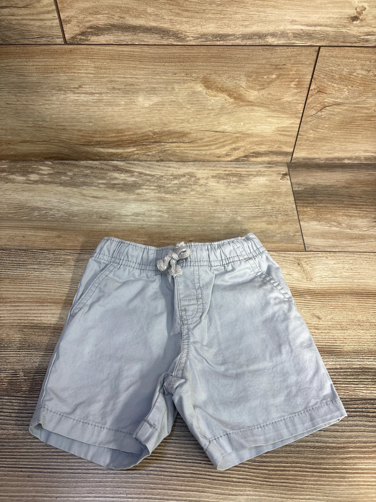 Top-down view of grey Cat and Jack toddler shorts, size 18 months, elastic waist with drawstring and pockets on wood floor