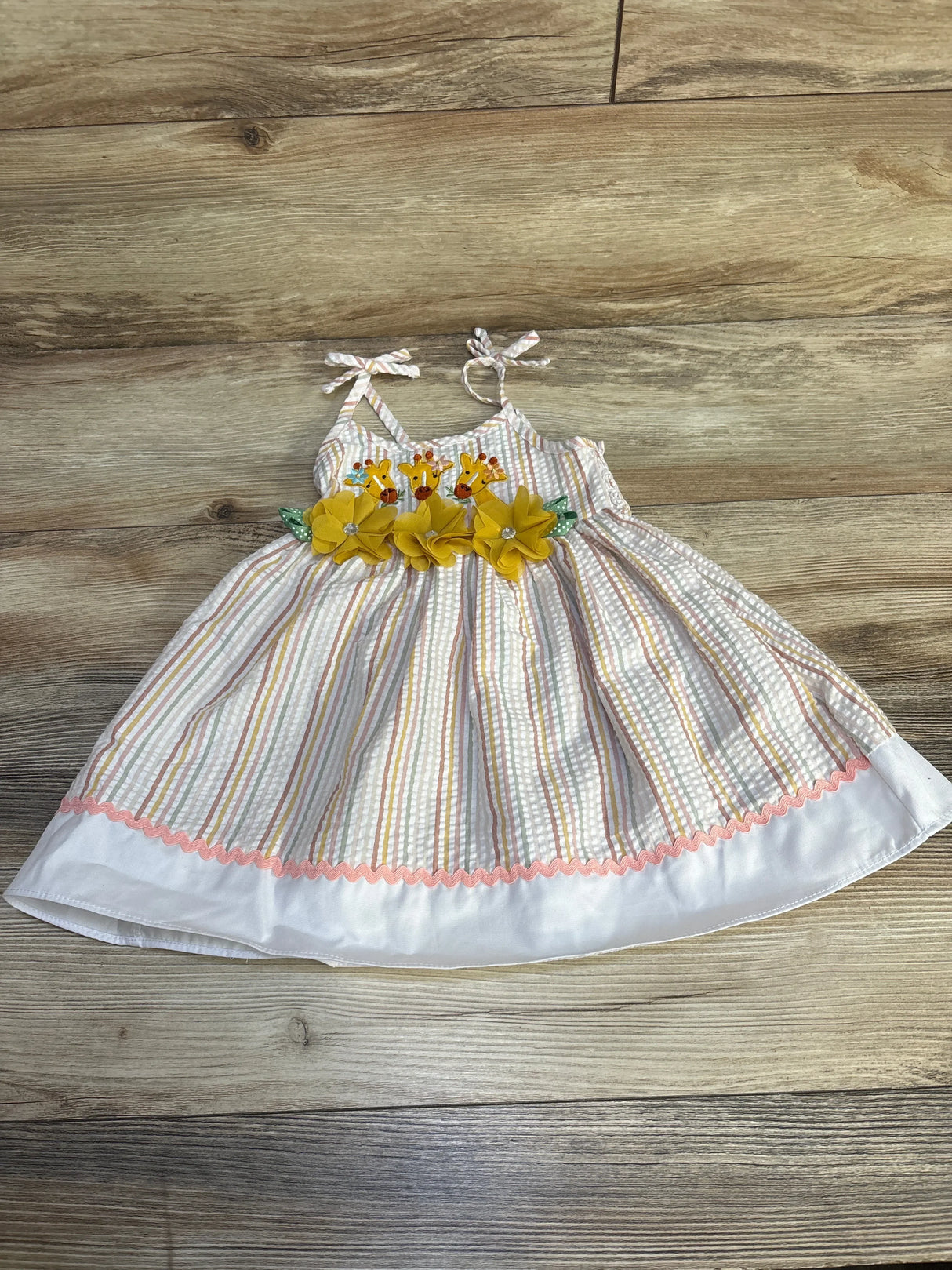 Flat lay of Goodlad gingham toddler sundress showcasing embroidered giraffes and yellow flower waistband on wood background