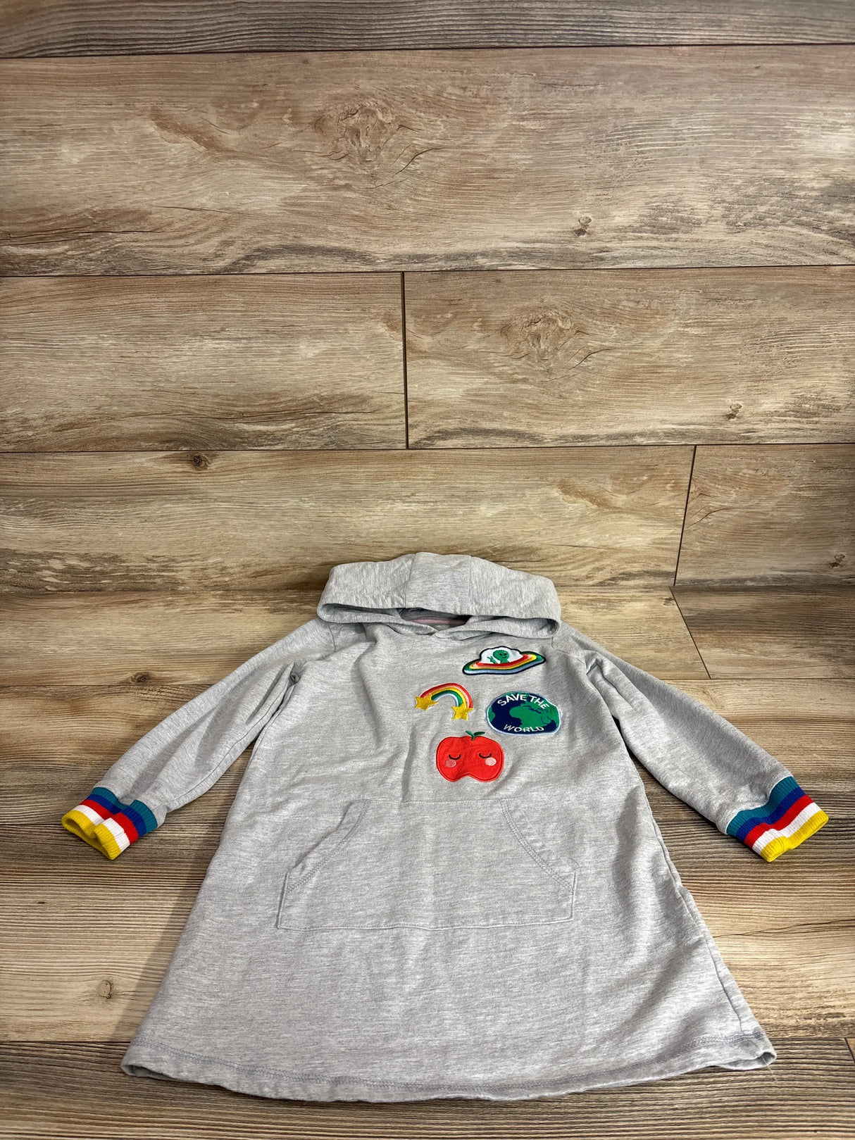 Flat lay of grey girls’ hooded patch sweater dress 4T with rainbow cuffs and ‘Save the World’ patch on wood