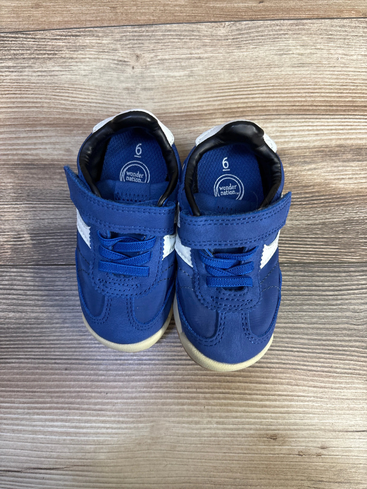 Top view of Wonder Nation toddler sneakers showing blue color, velcro strap, white side stripe, size 6C insole on wood floor