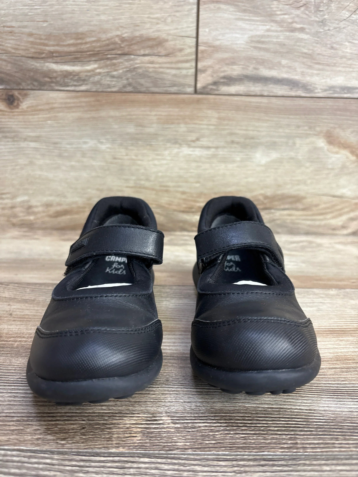 Black kids' Mary Jane shoes with Velcro straps on wooden floor